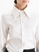 Camisa de jacquard con diseño de flores sutiles, color blanco, con cuello amplio de puntas marcadas, mangas largas con puños y cierre frontal con botones.