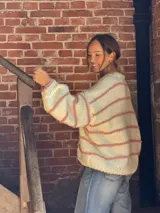 Buzo tejido de punto con silueta oversize, color crudo con rayas horizontales en color rosado. Presenta cuello redondo y mangas largas con caída relajada.