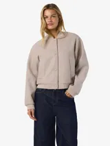 Campera bomber de corte holgado en color beige, con cuello redondo tipo baseball, cierre frontal con botones a presión, bolsillos laterales y puños y ruedo elastizados.