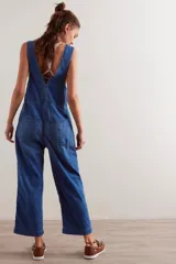 Enterito de denim azul con calce relajado, escote cuadrado, cierre frontal y diseño tipo jardunera con bolsillos.