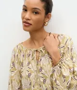 Blusa de manga larga con estampado geométrico en tonos verdes y violetas, cuello redondo con detalle de amarre frontal y puños elásticos.