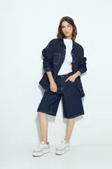 Bermuda de denim en color azul oscuro con diseño de rayas verticales blancas. Presenta un corte holgado, tiro medio y cierre frontal con botón y cremallera.