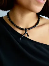 Collar tipo gargantilla compuesto por cuentas cilíndricas negras intercaladas con pequeñas esferas metálicas plateadas. Presenta un dije central con forma orgánica que simula una rama o coral en color negro.