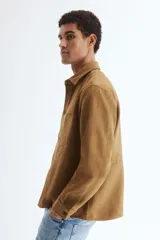 Sobrecamisa de H&M en tejido de efecto gamuza color marrón, con cuello inglés, cierre frontal de botones, un bolsillo en el pecho y mangas largas con puños abotonados.