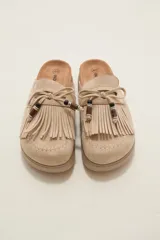 Suecos tipo mocasín color chocolate, confeccionados en material gamuzado. Presentan un diseño con flecos frontales, cordones decorativos con cuentas y una suela de plataforma plana de goma.