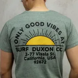 Remera verde jaspeado de algodón con cuello redondo y manga corta. Estampa en el pecho con un sol naciente y la frase "Only Good Vibes Surf Duxon Co.". Incluye bolsillo pequeño en el pecho.