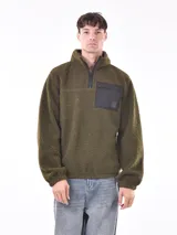 Buzo de polar verde oliva con cierre de medio largo y bolsillo de nylon negro en el pecho.