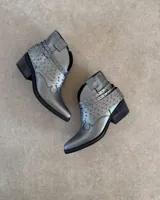 Botines cortos plateados de cuero vacuno, con punta fina, taco bajo y detalle de tachas y correas alrededor del tobillo.