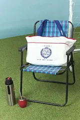 Bolso tipo tote de algodón en color blanco, con manijas azules y detalle de ribete rojo. Presenta un estampado frontal en azul con un diseño inspirado en el escudo nacional y texto alusivo.