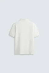 Polo de manga corta color blanco roto, con cuello solapa y cierre frontal de cremallera. Presenta un tejido de piqué estructurado y corte regular fit.