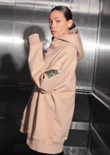 Buzo oversize color nude confeccionado en frisa, con capucha amplia, bolsillo canguro, terminaciones de puño y ruedo con rib, y logo de la marca bordado en el centro delantero.