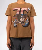 Remera de tejido suave color marrón con lavado especial, mangas cortas y cuello redondo. Presenta terminaciones con efecto desgastado en cuello, mangas y ruedo. Estampado frontal con el número "76" con diseño de bandera estadounidense, un águila calva con una cinta que dice "American Love" y estrellas.