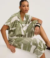 Pantalón tipo pantacourt confeccionado en viscosa con estampado de follaje verde sobre fondo blanco, con cintura elástica y diseño de pierna ancha y corta.