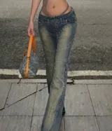 Jean de tiro bajo con efecto desgastado y costuras decorativas que realzan la silueta. Presenta un corte ajustado en la cadera y muslos con una leve apertura acampanada en la botamanga, incorporando un cierre frontal visible.