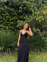 Vestido largo negro de corte bajo busto, con escote en V y top de tirantes finos cruzados en la espalda. Presenta falda larga con tajo lateral y detalles de volados de encaje.