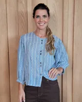 Camisa de manga larga con diseño de rayas verticales y bordados sutiles. Presenta cuello redondo, cierre frontal con botones y mangas abullonadas con volados en los hombros.