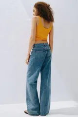 Jean de tiro alto confeccionado en denim de algodón lavado con diseño de cinco bolsillos, piernas rectas y holgadas, y detalles de roturas en las rodillas.