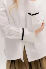 Camisa de manga larga color celeste claro, con cuello camisero y botones frontales. Presenta un detalle de cinta negra alrededor del puño doblado.