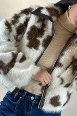 Campera corta de piel sintética con estampado de manchas tipo vaca en tonos blanco y marrón. Presenta cuello camisero, cierre frontal con cremallera y detalles en cuero sintético marrón en el cuello y la solapa del cierre.