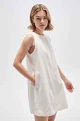 Vestido corto de jean blanco con tirantes anchos, cuello redondo, corte holgado y bolsillos laterales.