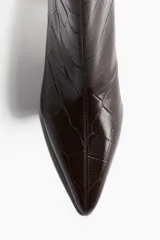 Botines cortos de mujer color marrón oscuro, con textura de cocodrilo en relieve y punta fina. Presentan un taco bajo y curvo, y un corte ajustado en el tobillo.