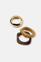 Pack de tres pulseras rígidas de diseño minimalista. Incluye dos brazaletes de resina con efecto carey en tonos marrón claro y oscuro, y un brazalete metálico de acabado dorado.