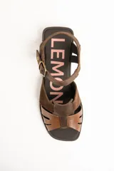 Sandalias de cuero color marrón, estilo romano, con tiras entrelazadas en la parte delantera y tira ajustable al tobillo con hebilla metálica.