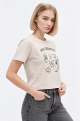 Remera de manga corta de algodón, color blanco, con cuello redondo y estampado frontal estilo collage con gráficos y texto en tono bordó.