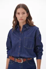 Camisa de jean azul oscuro, de corte recto, con cuello clásico, cierre frontal con botones metálicos envejecidos, manga larga con puños abotonados, un bolsillo de parche en el pecho y costuras a tono.