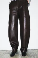 Pantalón de tiro medio con diseño tipo balloon, confeccionado en tejido efecto piel. Presenta bolsillos laterales, pespuntes marcados a tono y cierre frontal con cremallera, botón y gancho metálico.