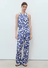Pantalón tiro medio de corte recto, con estampado floral azul sobre fondo blanco, detalle de pinzas y bolsillos laterales. Cierre oculto con botón, gancho y cremallera.