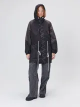 Campera tipo piloto con capucha, cierre frontal con botones y detalle de costuras en zigzag. Presenta cordones ajustables en la cintura y capucha, puños elásticos y logo bordado en el pecho.