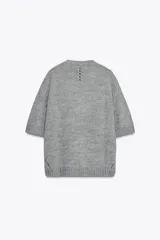 Jersey de punto color amarillo pálido, con cuello redondo y mangas cortas. Presenta un calce oversize y aberturas caladas en los laterales inferiores.