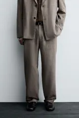 Pantalón de traje de corte slim fit, color marrón con textura sutil. Cuenta con cierre frontal de cremallera y botón, bolsillos laterales y bolsillos traseros de doble vivo con botón.