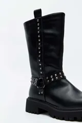 Bota alta negra de estilo biker, con suela track gruesa, detalles de tachas metálicas en las tiras del tobillo y a lo largo de la caña, y presilla trasera.