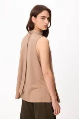 Blusa sin mangas color crema, con cuello alto fruncido y diseño holgado.