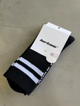 Medias largas negras con dos rayas blancas horizontales en la parte superior y detalles de costura blanca en el lateral.