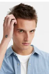 Camisa de manga corta estilo western, confeccionada en tejido chambray de algodón color celeste. Presenta cuello clásico, cierre frontal con botones a presión, dos bolsillos frontales con solapa y etiqueta roja distintiva de la marca.