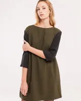 Vestido corto negro con mangas 3/4 verdes, cuello bote y bolsillos laterales.