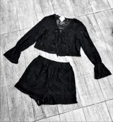 Conjunto de encaje negro, compuesto por un top corto con mangas acampanadas y cordones en el frente, y un short con cintura elástica.