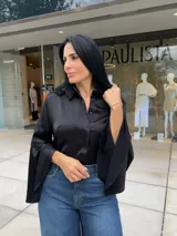 Blusa negra de manga larga con cuello camisero y puños acampanados o con aberturas.