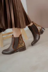 Botinetas de cuero color marrón con diseño tipo chelsea, con paneles laterales elásticos y detalle de cuero texturizado con acabado metalizado en el talón. Poseen taco bajo cuadrado y terminación redondeada.