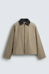 Sobrecamisa de corte relajado color beige, con cuello solapa en efecto piel de color negro. Presenta cierre frontal con cremallera, bolsillos de vivo en la cadera y mangas largas con puños ajustables.