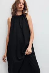 Vestido midi de color marrón con acabado satinado, cuello redondo con detalle fruncido y diseño sin mangas. Presenta un corte fluido con bajo asimétrico y bolsillos laterales ocultos.