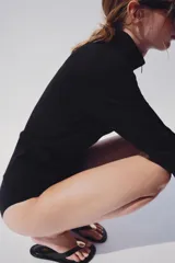 Chaqueta de punto negra con cuello subido y cierre frontal con cremallera, de manga larga y diseño ajustado.