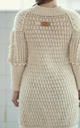 Cárdigan largo color crudo tejido a crochet en lana merino, con cuello en V, cierre frontal con botones de guampa tallados a mano, mangas largas con trenzas 3D y puños extra largos.