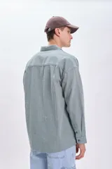Sobrecamisa verde con rayas verticales blancas, de corte holgado, manga larga, cuello camisero y dos bolsillos frontales con solapa.