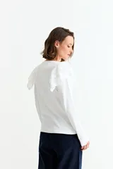 Remera de manga larga en color crudo, confeccionada en tejido acanalado, con detalle de volados en los hombros y cuello redondo.