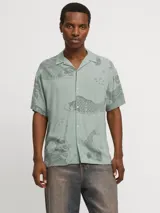 Camisa de viscosa LENZING™ ECOVERO™ color verde con estampado de peces y olas en gris, cuello resort, mangas cortas y corte relajado.