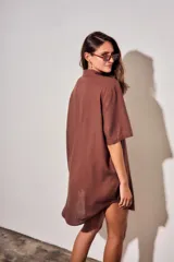 Vestido camisero corto de color marrón, con mangas cortas, cuello camisero, cierre frontal de botones y un bolsillo ojal en el pecho.
